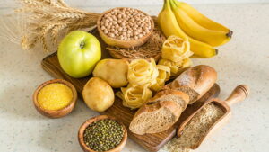 A cutting board with bread, beans, green apples, bananas, and wheat