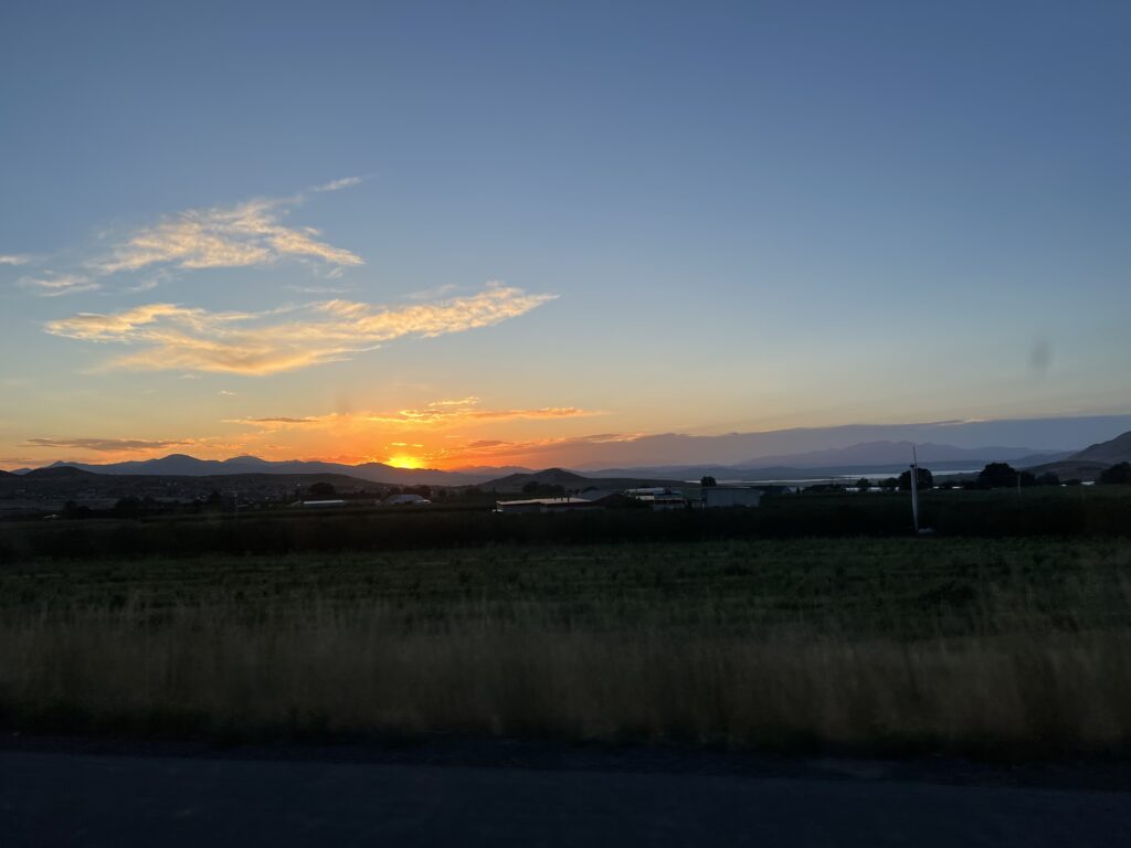 The sun sets behind low hills.